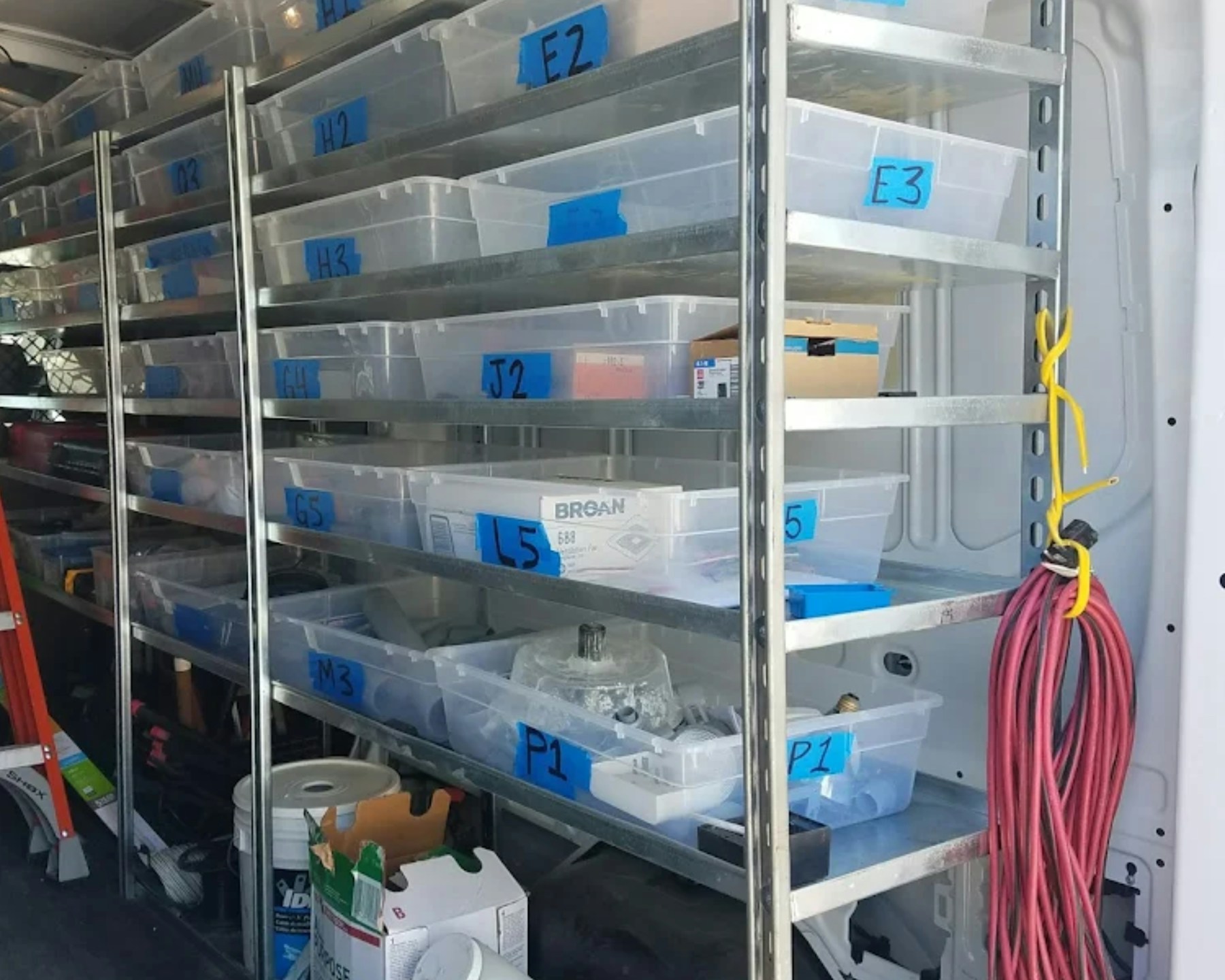 Inside an HVAC service van — labeled parts bins, ladder, and tools staged for the day's calls